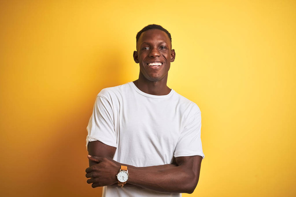 Young african american man wearing white t-shirt standing over isolated yellow background happy face smiling with crossed arms looking at the camera. Positive person. - Photo, Image