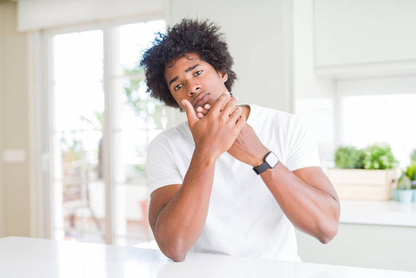Hombre afroamericano joven con camiseta blanca casual sentado en casa con dolor en las manos y los dedos, inflamación de la artritis
 - Foto, Imagen