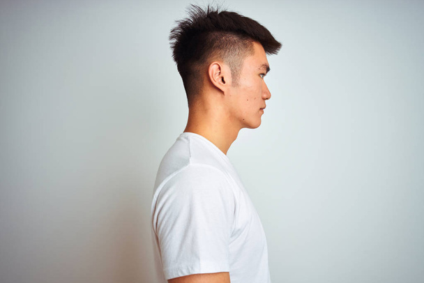 Młody Asian Chinese mężczyzna ubrany t-shirt stojący na białym tle patrząc na bok, relaks profil stwarzają z naturalną twarzą i pewny siebie uśmiech. - Zdjęcie, obraz