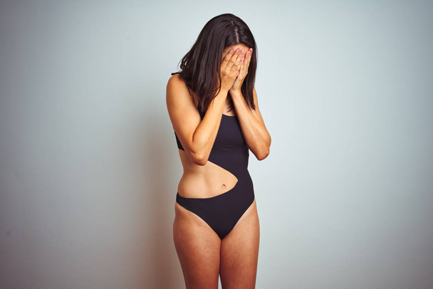 Beautiful woman wearing bikini swimwear over white isolated background with sad expression covering face with hands while crying. Depression concept. - Fotoğraf, Görsel