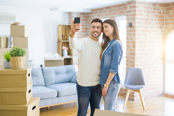 Όμορφο ζευγάρι παίρνοντας μια φωτογραφία selfie χρησιμοποιώντας smartphone σε νέο διαμέρισμα, χαμογελαστή χαρούμενη για το νέο σπίτι - Φωτογραφία, εικόνα
