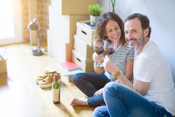 Średnim wieku starszy romantyczna para w miłości siedzi na podłodze w mieszkaniu z pudełka wokół, obchodzi picia kieliszek wina uśmiechnięty szczęśliwy do przejścia do nowego domu - Zdjęcie, obraz