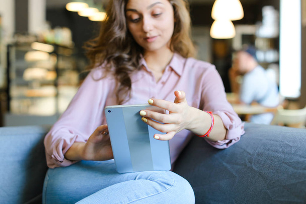 Mladá šťastná dívka sedí na pohovce v kavárně a používá tablet. - Fotografie, Obrázek