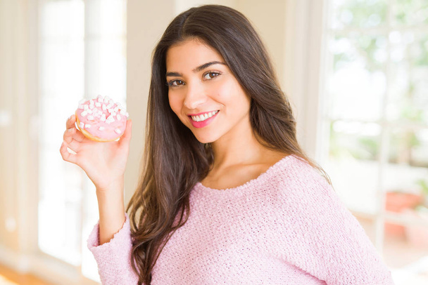 Молода красива жінка їсть рожевий смачний пончик посміхається
  - Фото, зображення
