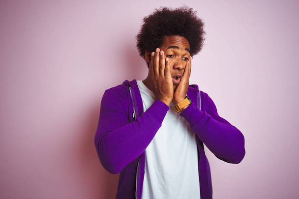 Молодий афроамериканець чоловік носить фіолетовий Толстовка стоячи над ізольованою рожевий фон втомився руки охоплюють обличчя, депресії і смутку, засмучений і роздратований для вирішення проблеми - Фото, зображення