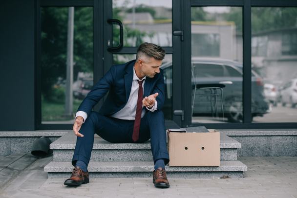 dismissed businessman sitting on stairs and looking at carton box  - Photo, Image