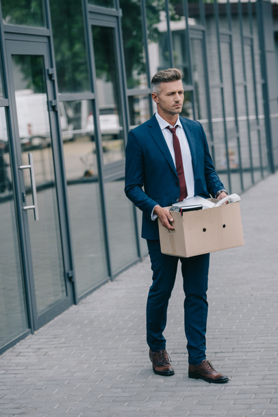 ontslagen zakenman wandelen in de buurt van gebouw en houden kartonnen doos  - Foto, afbeelding