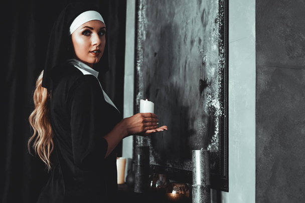 Young catholic nun is holding candle in her hands. Photo on black background - Photo, Image