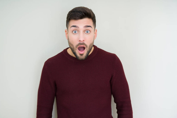 Young handsome man wearing a sweater over isolated background afraid and shocked with surprise expression, fear and excited face. - Photo, Image