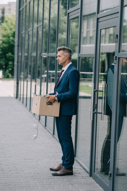 vista lateral del hombre despedido en traje de pie cerca del edificio con teléfono retro en caja de cartón
  - Foto, imagen