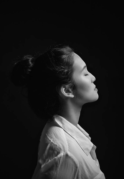 Lato della donna con i peli dei panini che indossa una camicia bianca a maniche lunghe Faccia in su alla luce su uno sfondo nero
 - Foto, immagini