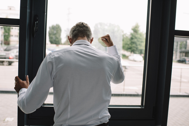visão traseira do empresário de pé com o punho cerrado perto de janelas
 - Foto, Imagem