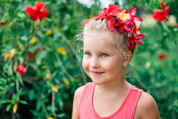 Cute smiling little girl portrait in summer garden with red flowers. - Valokuva, kuva