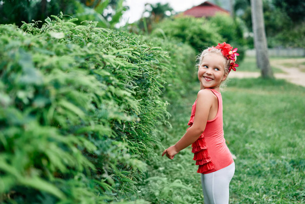 Cute smiling little girl portrait in summer garden with red flowers. - Photo, Image