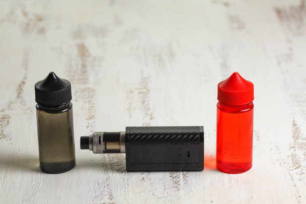 Vape objects. Electronic cigarette and jars with e-liquid on a light wooden table. - Fotoğraf, Görsel