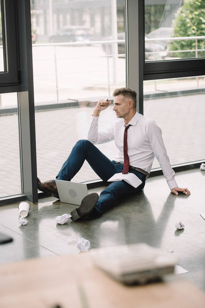 вибірковий фокус бізнесмена, що сидить на підлозі біля вікон
  - Фото, зображення