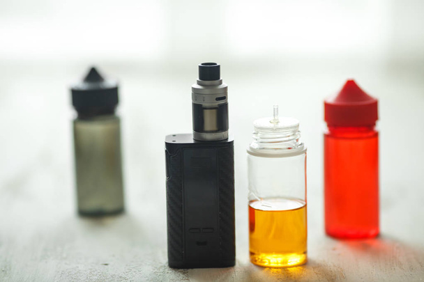 Vape objects. Electronic cigarette and jars with e-liquid on a light wooden table. - Foto, Imagem