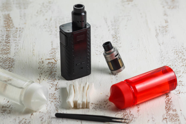 Vape objects. Electronic cigarette and jars with e-liquid on a light wooden table. - 写真・画像