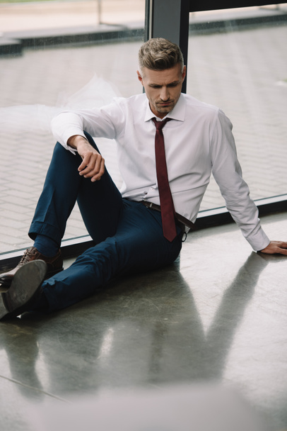 turhautunut liikemies istuu lattialla lähellä ikkunat toimistossa
  - Valokuva, kuva