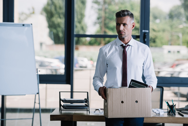 избирательный фокус привлекательного бизнесмена, держащего коробку рядом с рабочим местом
  - Фото, изображение