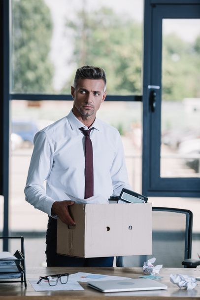 serious businessman holding box while standing near workplace  - Photo, Image