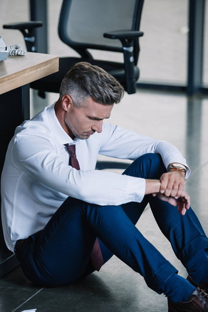 upset businessman sitting on floor near workplace in office  - Фото, зображення