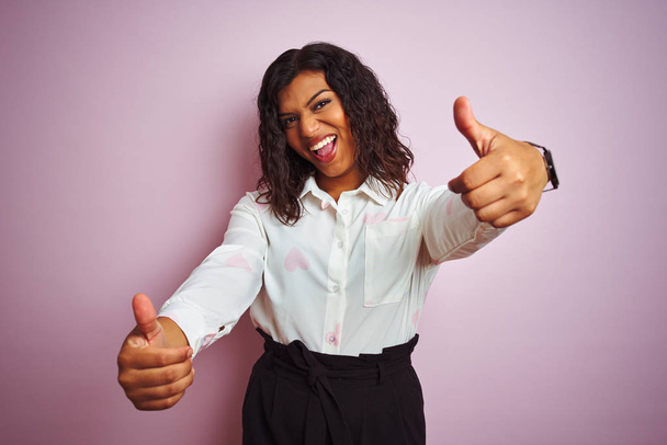 Transsexual transgender businesswoman standing over isolated pink background approving doing positive gesture with hand, thumbs up smiling and happy for success. Winner gesture. - Fotó, kép