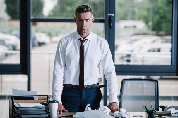 serious businessman looking at camera near desk in office  - Foto, Imagen
