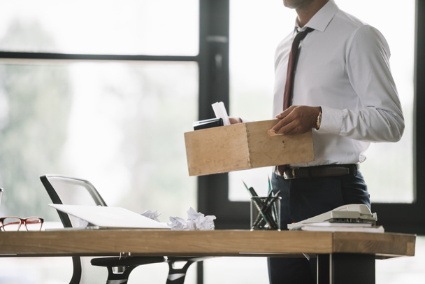cropped view of dismissed businessman holding wooden box in modern office  - Photo, Image