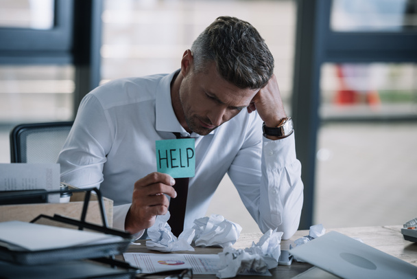 selective focus of upset businessman holding sticky note with help lettering near table  - Photo, Image