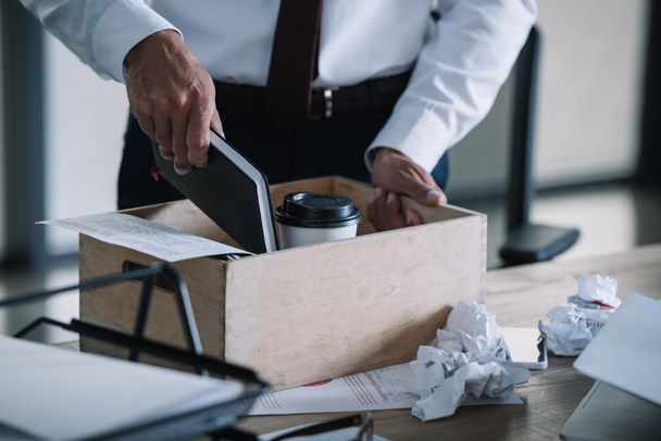 περικομμένη θέα του ανθρώπου βάζοντας σημειωματάριο σε ξύλινο κουτί κοντά σε χάρτινο κύπελλο και τσαλακωμένα μπάλες χαρτιού στο τραπέζι  - Φωτογραφία, εικόνα
