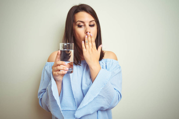 Mladá krásná žena pije sklenici čerstvé vody na izolované pozadí a s rukama šokovanou hanbou o omyl, projev strachu, strach v tichosti, tajný koncept - Fotografie, Obrázek
