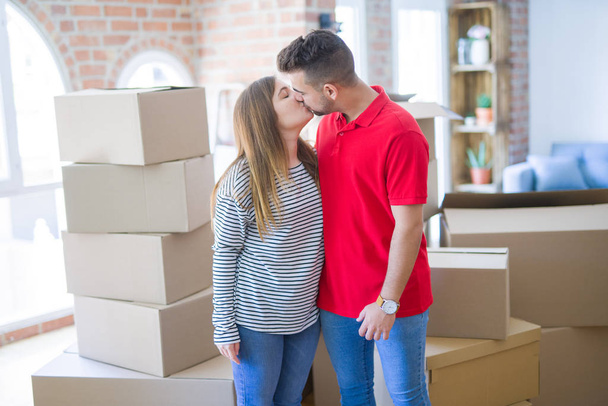 Young beautiful couple in love around cardboard boxes moving to new home, smiling very happy and cheerful for new apartment - Фото, изображение