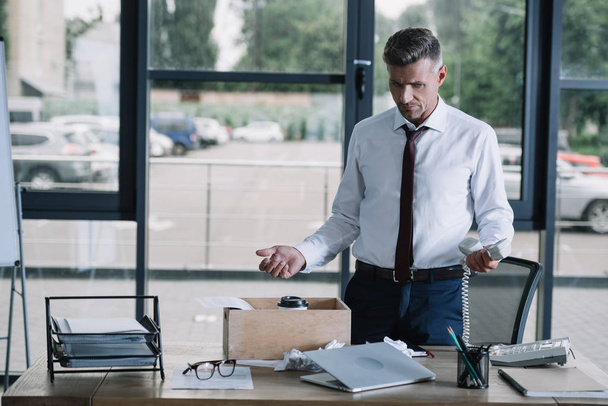 бизнесмен в формальной одежде жестикулирует у стола в офисе
  - Фото, изображение