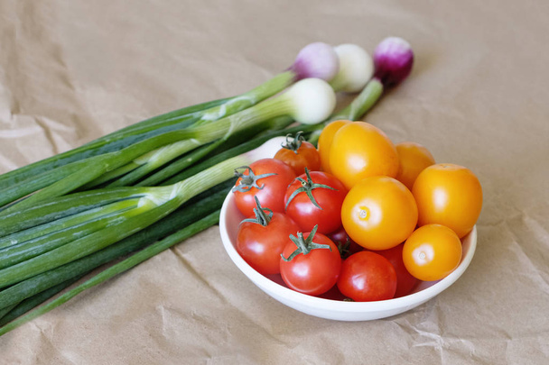 Vihanneksia paperilla taustalla. Luomuruokaa ja tuoreita vihanneksia. Kevätsipulit, kirsikkatomaatit ja munat pöydällä
. - Valokuva, kuva
