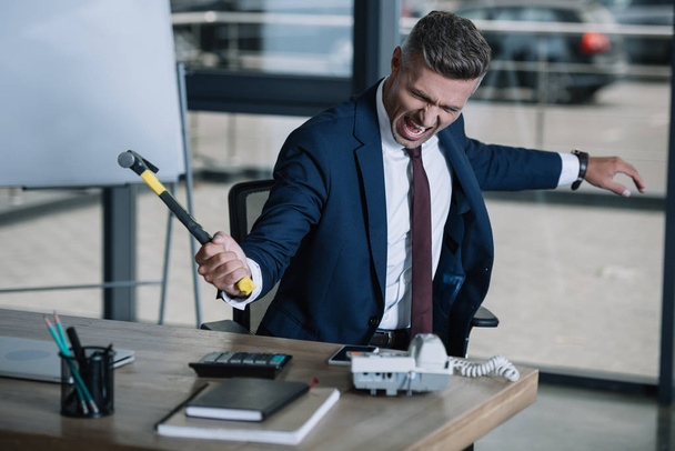 selective focus of angry businessman holding hammer near table  - Фото, зображення