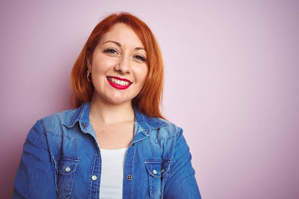 Youg beautiful redhead woman wearing denim shirt standing over isolated pink background happy face smiling with crossed arms looking at the camera. Positive person. - Foto, imagen