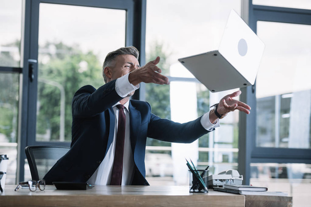 емоційний бізнесмен кидає в повітря ноутбук в офісі
  - Фото, зображення