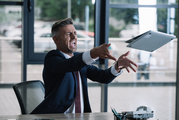 Wütender Geschäftsmann wirft Laptop in Büro  - Foto, Bild