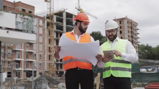 Building a residential complex or business center. Team of engineers men with a tablet and drawing analyzing plans construction builders job activity. - Кадри, відео