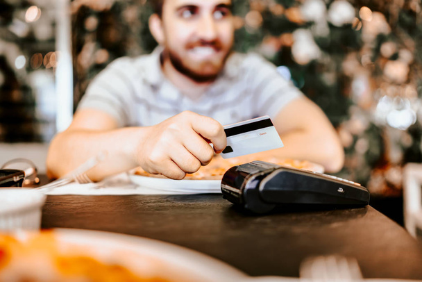 close up portrait of man paying with credit card at restaurant. Focus on hands, card and payment terminal - Photo, image