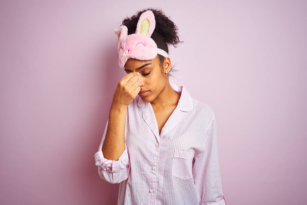 Młoda African American kobieta noszenie piżamy i maski na białym tle różowy zmęczony tarcie nos i oczy uczucie zmęczenia i bóle głowy. Koncepcja stresu i frustracji. - Zdjęcie, obraz
