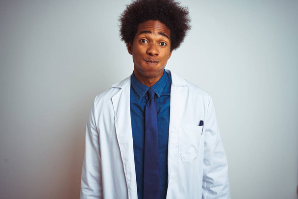 Mladý Afričan americký doktor na sobě nosí kabát stojící nad osamělé bílé pozadí s veselenou tváří. Ústa nafouknutými vzduchem, šíleným výrazem. - Fotografie, Obrázek