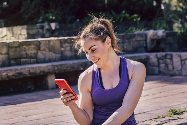 smiling sporty woman sitting looking at the phone - Foto, Bild