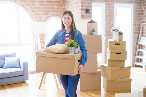 Красивая азиатская молодая женщина держит коробки, улыбаясь счастливый переезд
  - Фото, изображение