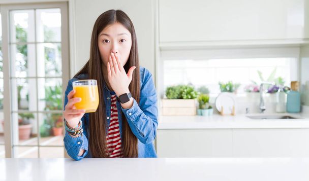 Красива Азіатська жінка питної склянку свіжого апельсинового соку охоплюють рот з боку вражений з ганьбою за помилку, вираз страху, злякавшись в тиші, Секретна концепція - Фото, зображення
