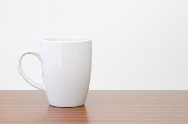 White mug on dark wooden table with white wall - Fotoğraf, Görsel