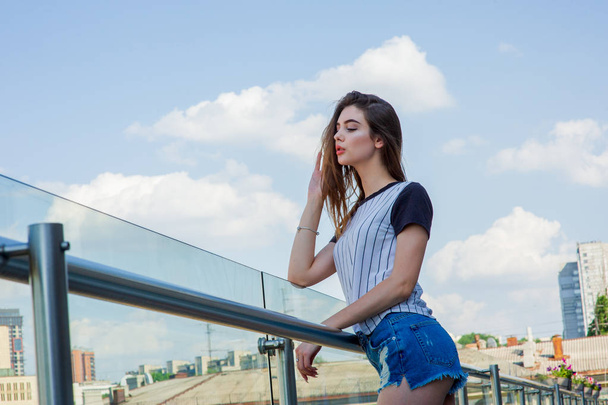 Ragazza in pantaloncini sul balcone in un bar. Ritratto estivo di giovane ragazza elegante in posa sul balcone, mini pantaloncini di jeans
 - Foto, immagini