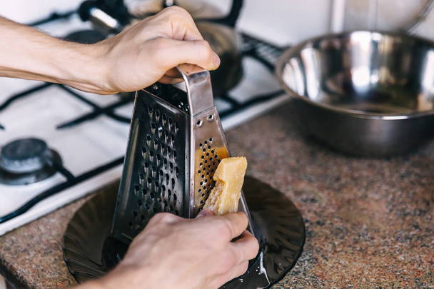 man holds a piece of parmesan cheese and rubbed on a grater. kit - Valokuva, kuva