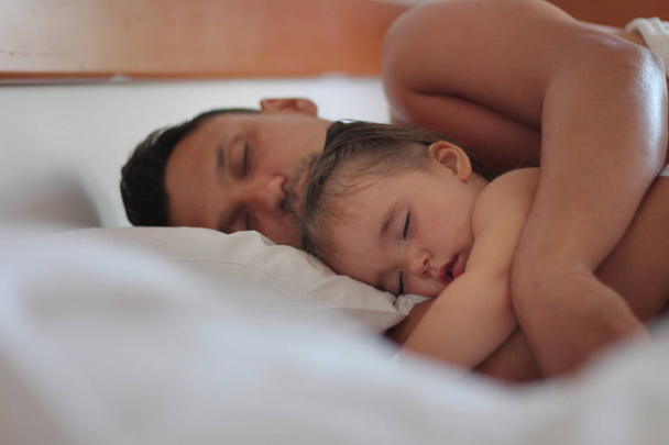 Dad hugs his daughter in a dream. A man and a child sleeping on white pillow - Valokuva, kuva